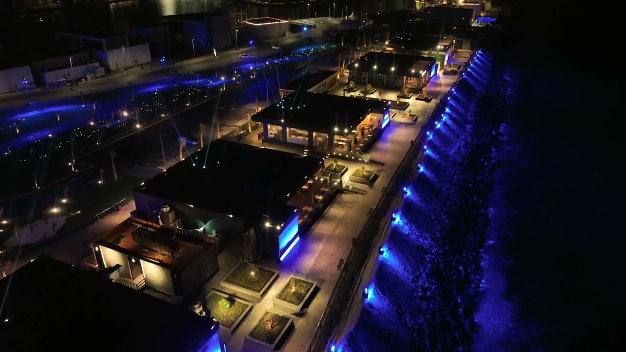 Aerial view of Luna's waterfront, with warm dining terraces, a blue-lit shoreline and white beams above the venue.